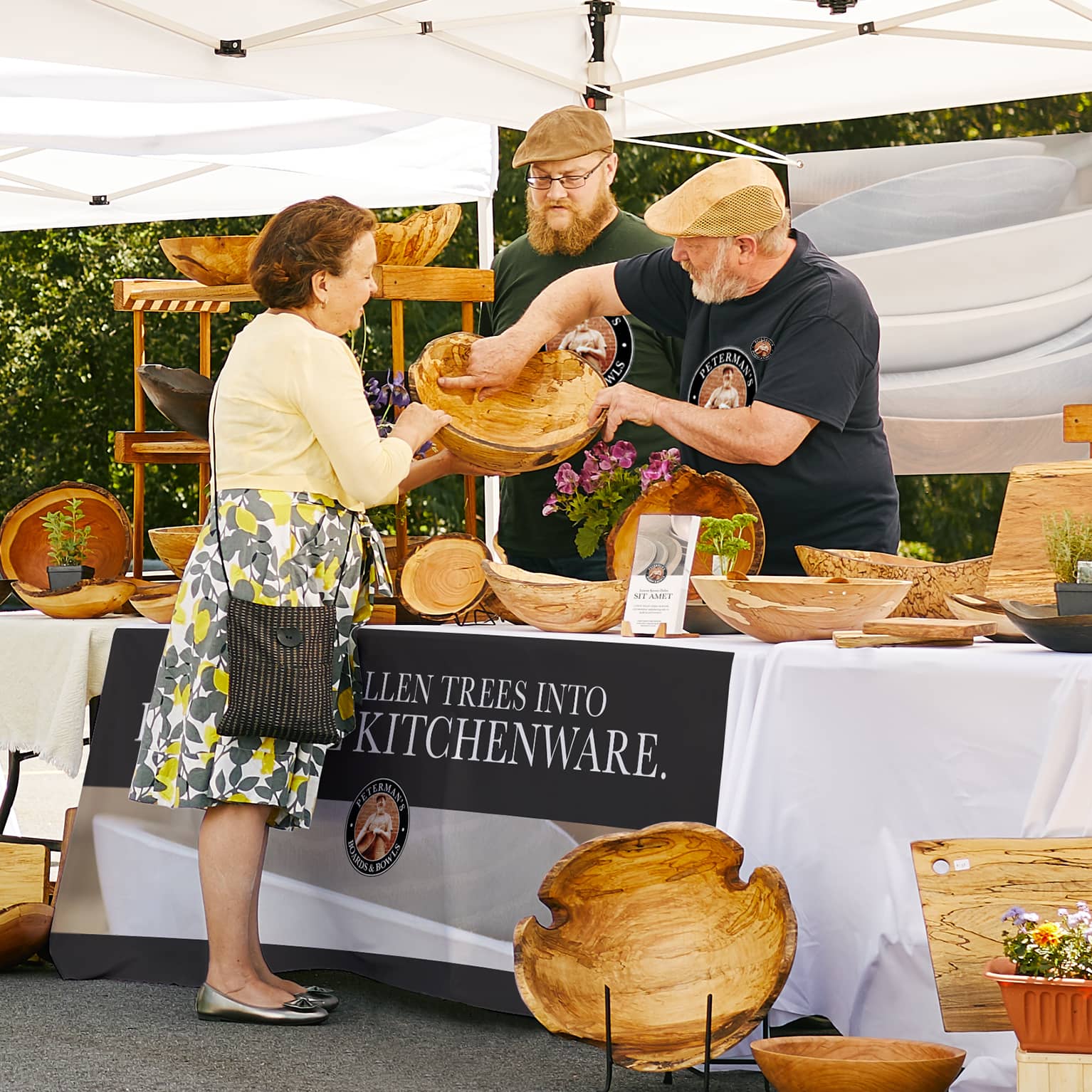 Vendor presenting handcrafted wooden kitchenware to a customer at an outdoor market stall with bowls and home goods on display