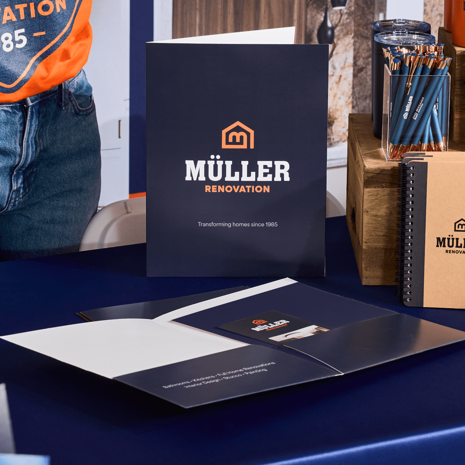 Branded folder, event QR code notebook and pens arranged on a table at a corporate event booth with visible company logo
