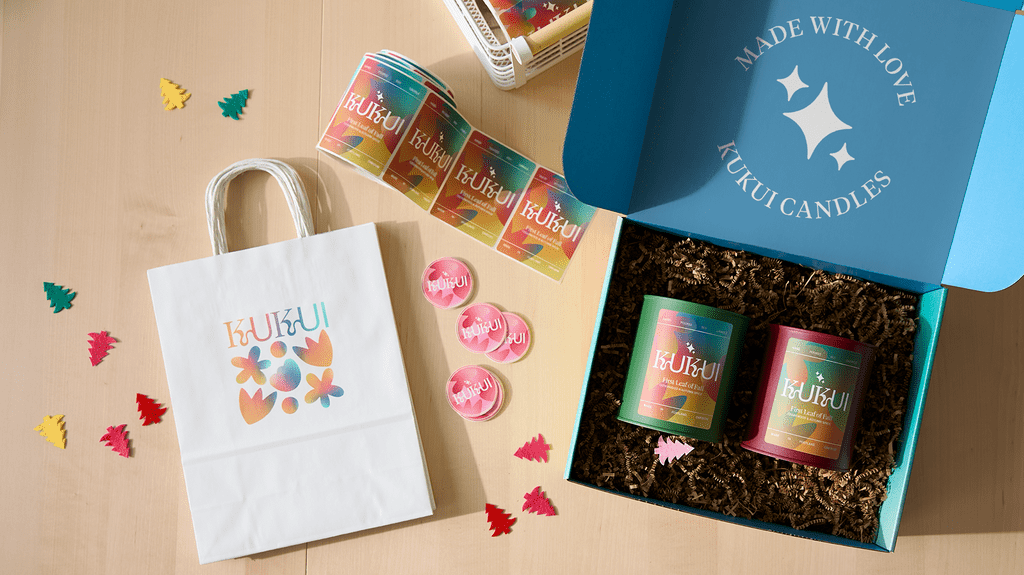 Branded candle gift packaging with a custom mailer box, paper shopping bag, stickers and colorful candle containers arranged with decorative holiday elements.