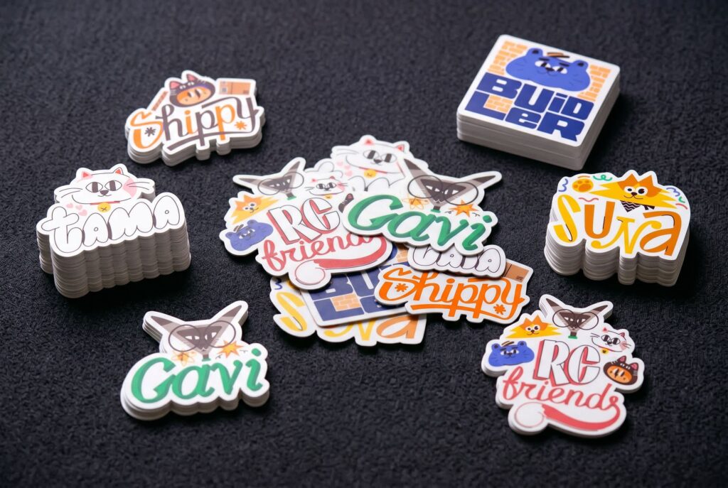 Assorted micro-merch stickers for Revenue Cat including standard square stacks and custom die-cut shapes, showing the contrast between simple formats and more expressive, irregular designs