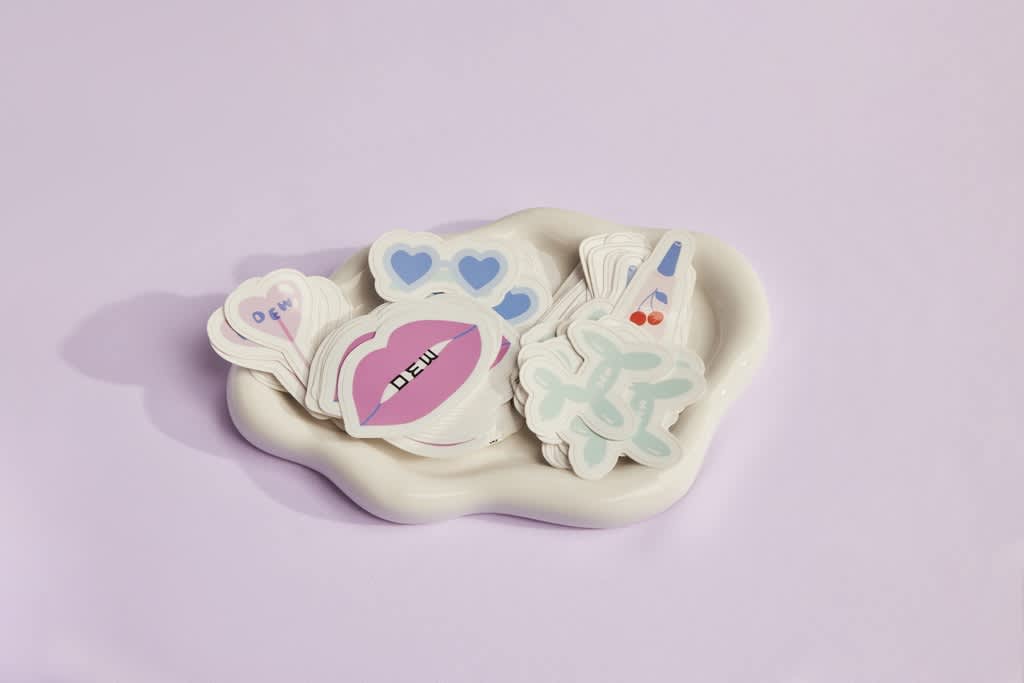 Assortment of colorful branded die-cut stickers with playful shapes and pastel colors arranged in a tray, showcasing varied designs within a cohesive visual style