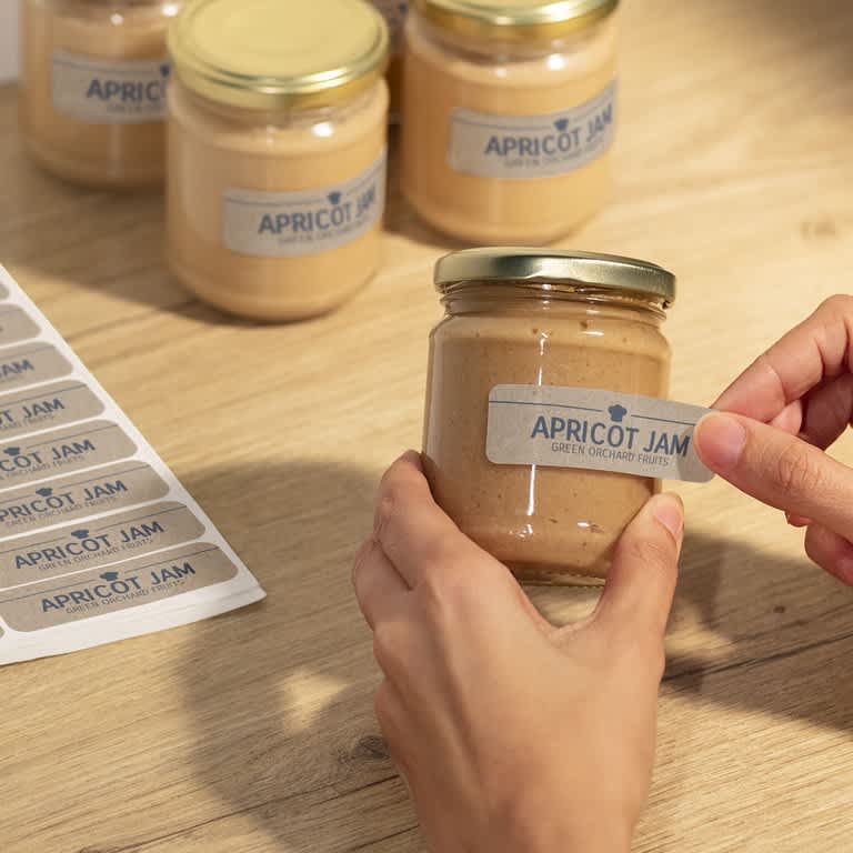Applying label to apricot jam jar with clean, minimal typography and simple product naming design.