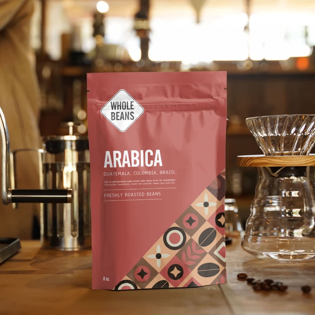 Matte coffee bag labeled Arabica standing on a wooden counter next to a pour-over setup in a caf&eacute;.