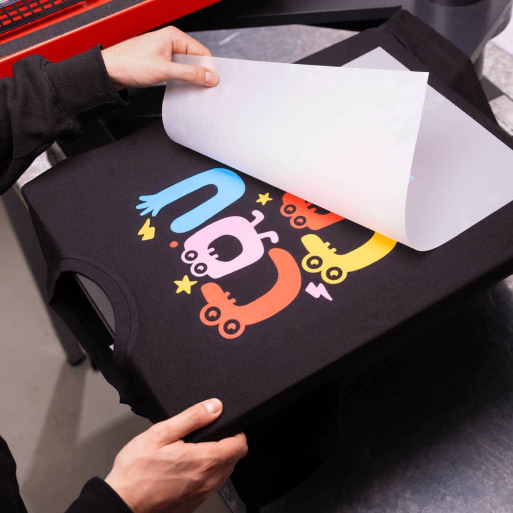 A sheet being peeled off a black T-shirt with bright print design.