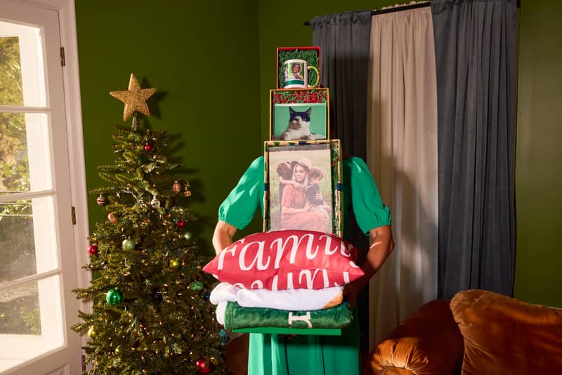 A person holding a stack of personalized Christmas gifts next to a decorated Christmas tree