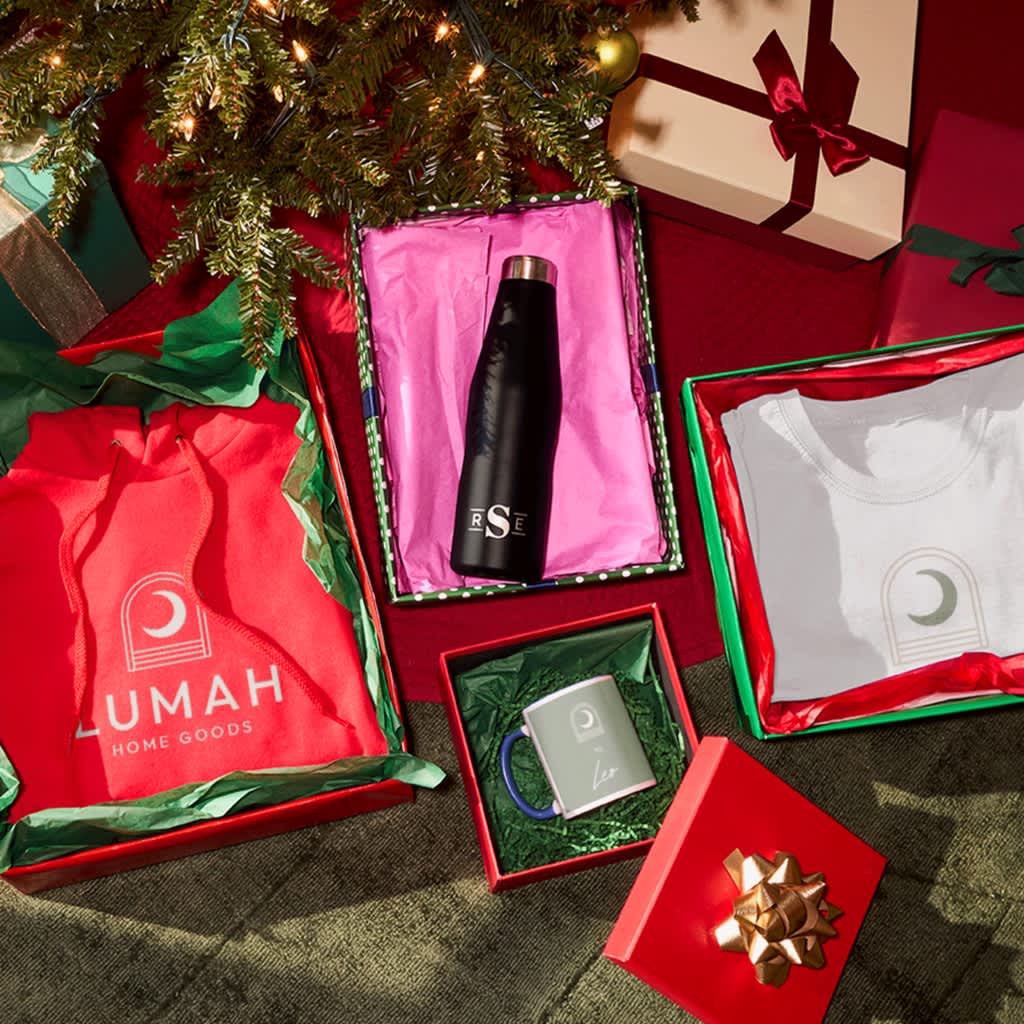 Boxed branded holiday gifts with colorful tissue paper under a tree.