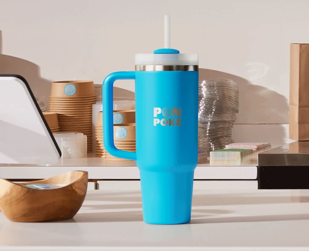 Branded blue travel mug on a shelf with a silver Pon Poke logo.