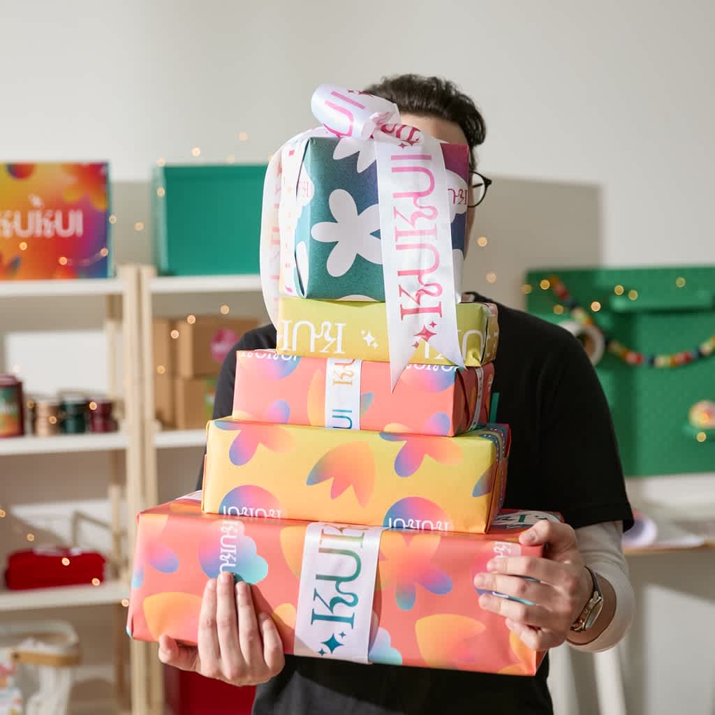 Man carrying a stack of gifts with branded wrapping paper and ribbon.