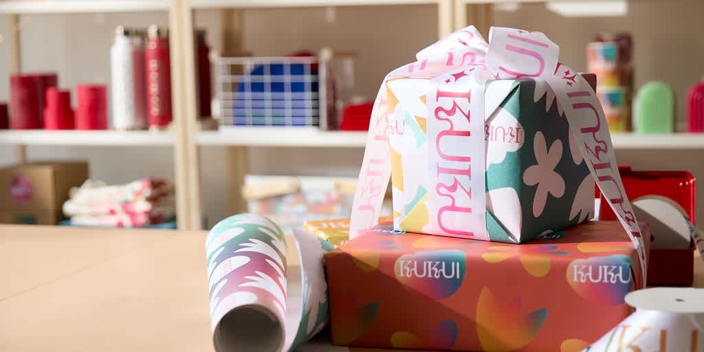 Stack of gifts in custom VistaPrint wrapping paper in front of a Christmas tree.