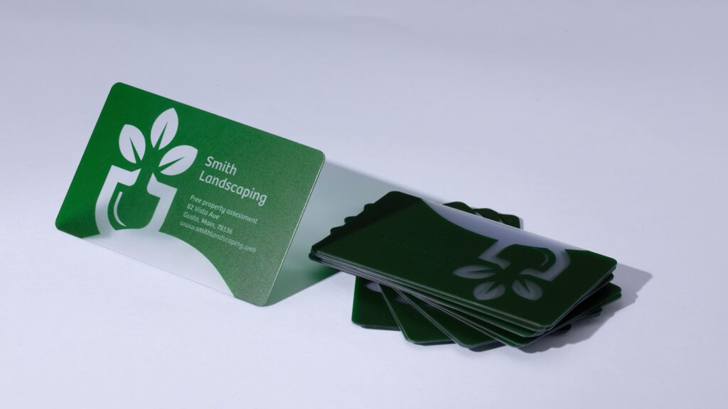Green plastic business cards for a landscaping company with a bold white logo, small contact text and rounded corners.