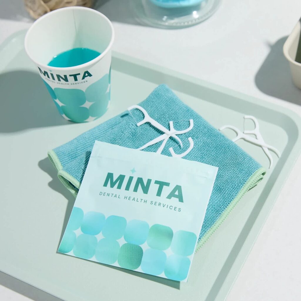  Custom MINTA Dental Health Services flat pouch with turquoise branding, displayed on a tray alongside dental floss picks, a towel and a branded cup.