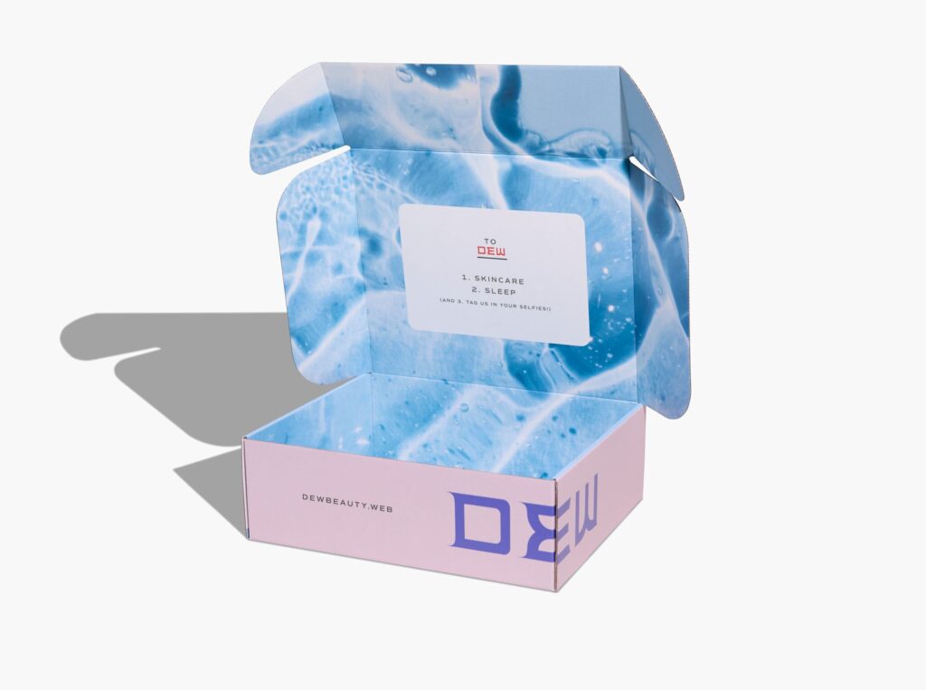 Open DEW Beauty custom mailer box with a blue water-patterned interior, pink exterior and a printed message encouraging customers to tag the brand in their selfies.