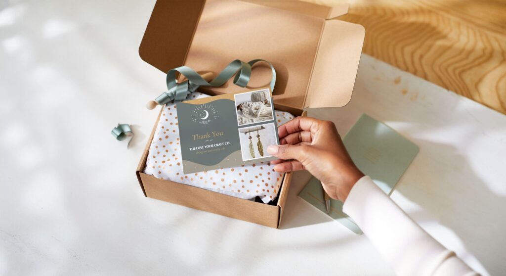 Person holding a branded thank-you card above an open kraft gift box containing a tissue-wrapped product, decorative ribbon and jewelry care insert.