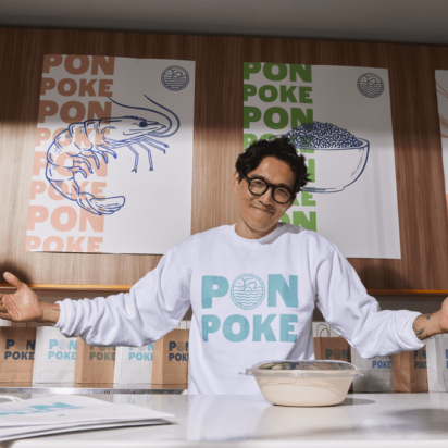 Employee wearing branded shirt standing in front of colorful restaurant posters — example of effective poster design.
