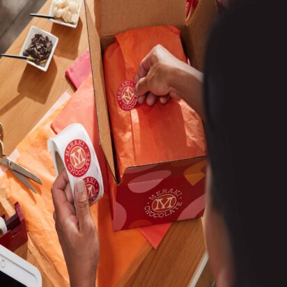 Person applying Meraki Chocolate branded stickers to holiday shipping packages.