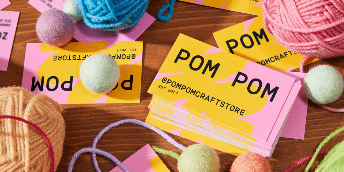 Colorful PomPom business cards scattered on a table with yarn balls – inspiration for how to design a business card.