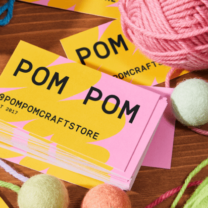 Colorful PomPom business cards scattered on a table with yarn balls – inspiration for how to design a business card.