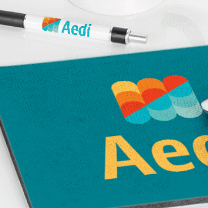 Branded merchandise on a white desk including a mug, USB stick, pen, and mousepad printed with a colorful logo