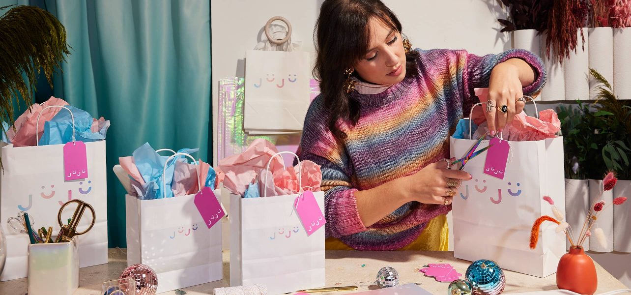 A small business owner packages products in branded shopping bags.