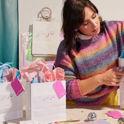 A small business owner packages products in branded shopping bags.
