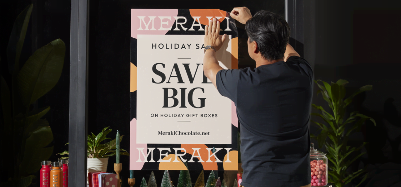 Small business owner applying a holiday sale decal to shop window – Christmas signage ideas in action.