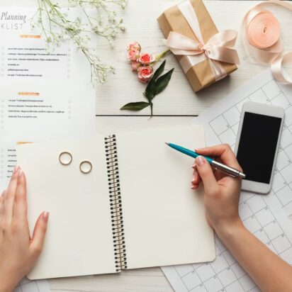 Wedding planning checklist with notebook, pen, rings and calendar on a desk