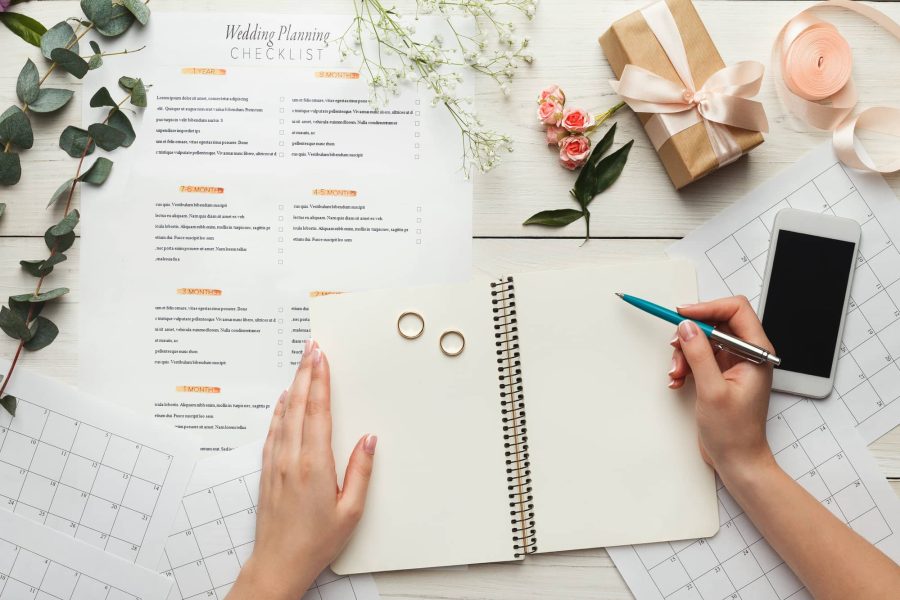 Wedding planning checklist with notebook, pen, rings and calendar on a desk