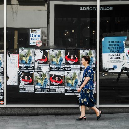 woman walking past window of posters