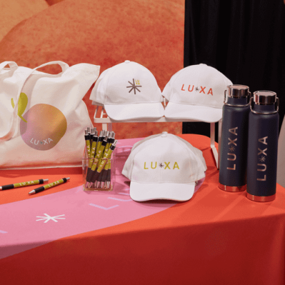 caps, tote bag and bottles all displaying branded print on colorful tradeshow desk
