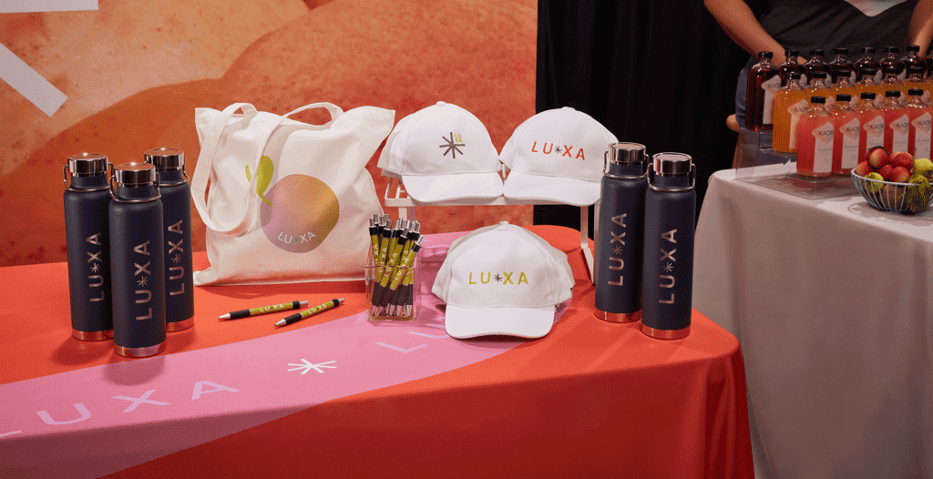 caps, tote bag and bottles all displaying branded print on colorful tradeshow desk