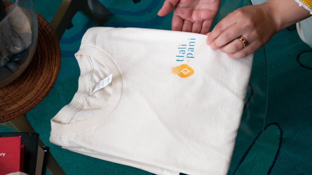 hands holding white branded t shirt for "tali pani" brand