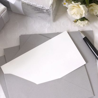 Writing paper or wedding invitation with envelope laid on bridal lace with several wedding gifts and white rose bouquets. Space for copy.