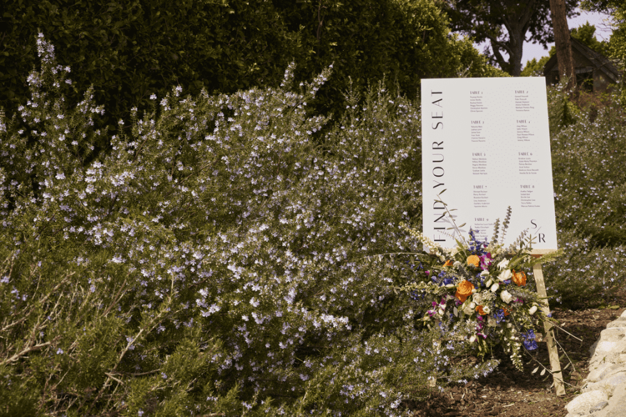 wedding seating chart sign decorated with flowers next to a bush