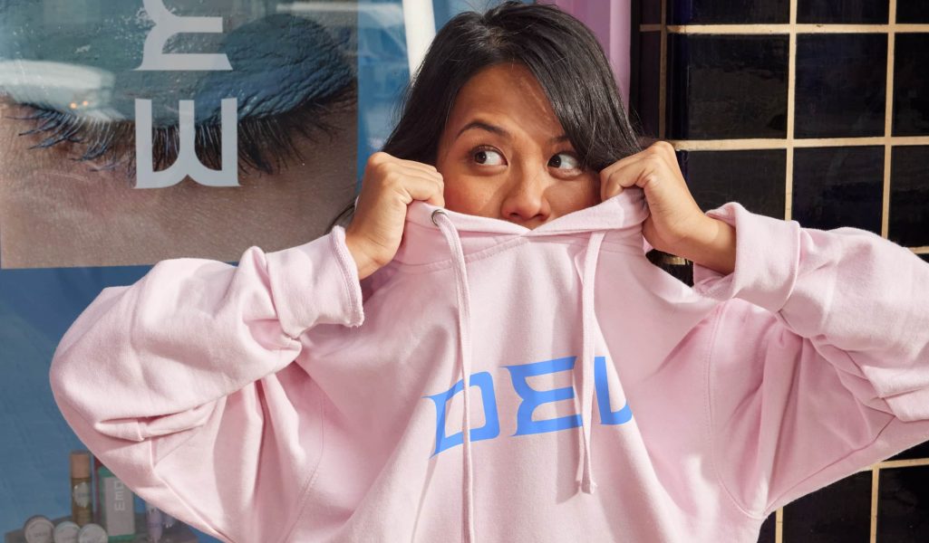 person peeks head above pink hoodie as they lift it over their head