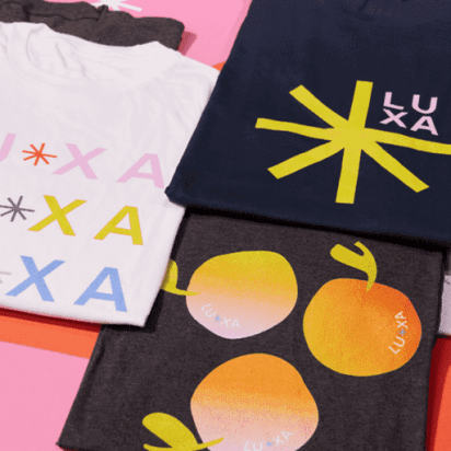 Promotional T-shirts in various colors with bold logos and text on a pink gradient background.