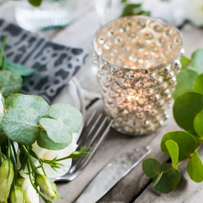 Table decor with white flowers, candles and glasses on old vintage rustic wooden table. Vintage summer wedding table decoration.