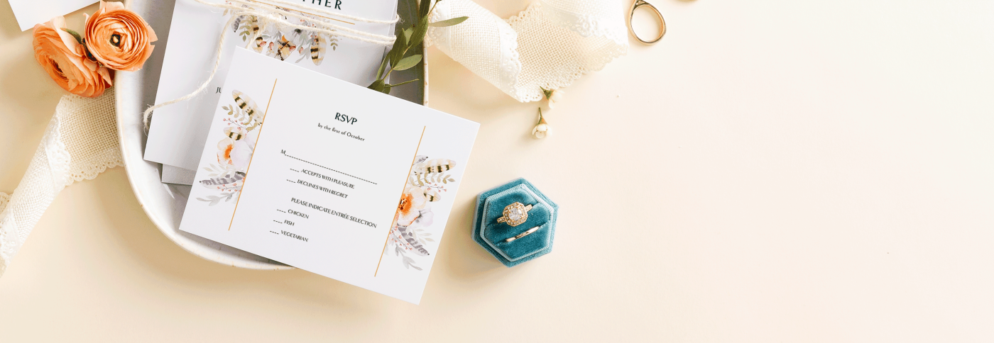 Elegant beige table with wedding RSVP cards on porcelain plate, decorated with roses, lace ribbons, and wedding rings.