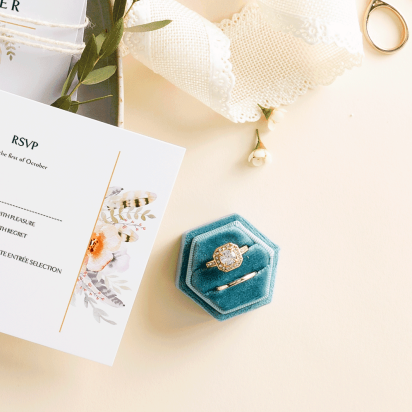 Elegant beige table with wedding RSVP cards on porcelain plate, decorated with roses, lace ribbons, and wedding rings.