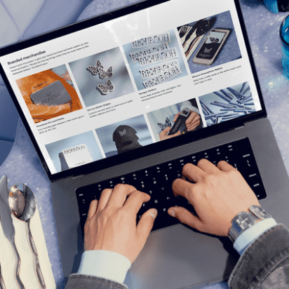 A person working on a laptop in a cozy environment, surrounded by everyday items like a cup of coffee and a notepad.