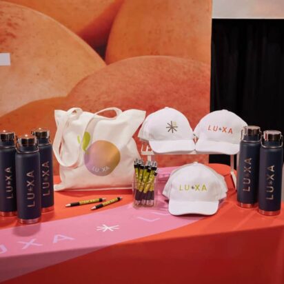 Branded merchandise display with custom tote bags, hats, water bottles and promotional items at marketing event