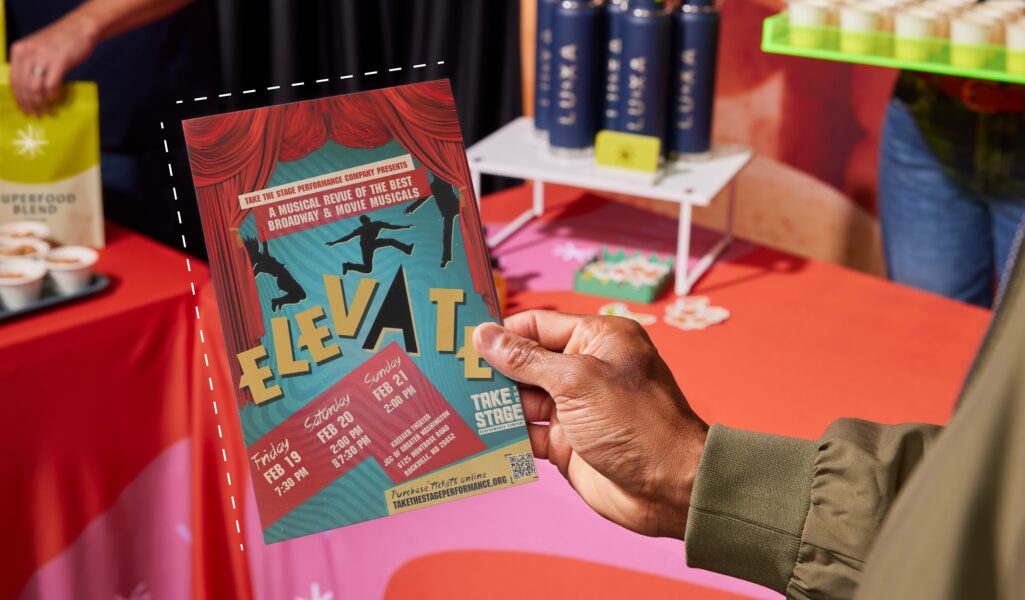 Person holding a colorful event flyer with bold typography and performance details at a promotional table