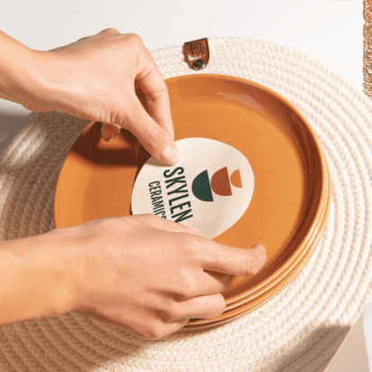 Hands applying a ceramic brand sticker to a red plate, showcasing logo design software in action.