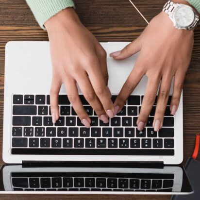 Hands typing on a laptop surrounded by stationery, coffee cup, and smartphone – web pages design software in use.