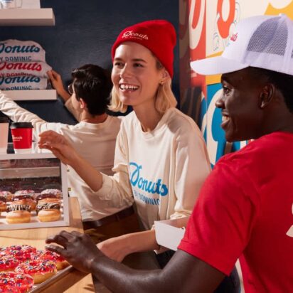 Two smiling employees behind the counter of a colorful donut shop, wearing branded accessories – part of the VistaPrint Small Business Happiness Report.