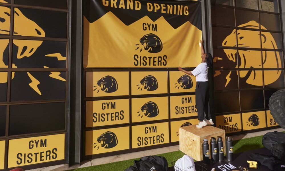 Small business owner hanging a branded Gym Sisters banner on her gym’s storefront window.