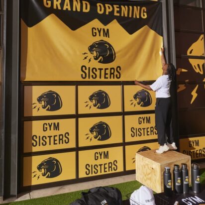 Small business owner hanging a branded Gym Sisters banner on her gym’s storefront window.