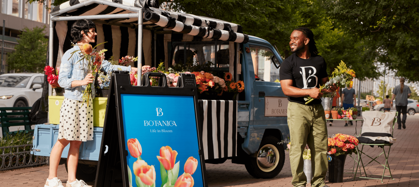 Colorful flower stand with smiling business owner, branded A-frame sign, and decorative pillows – inspiring business sign ideas.