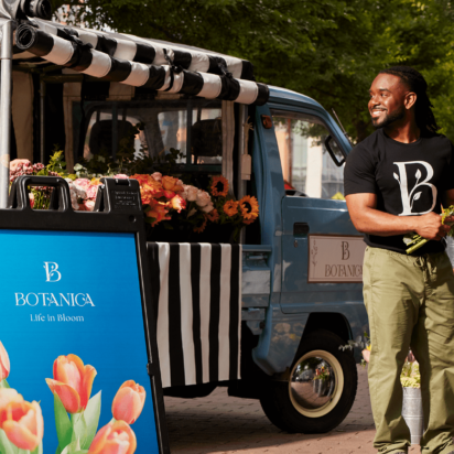 Colorful flower stand with smiling business owner, branded A-frame sign, and decorative pillows – inspiring business sign ideas.