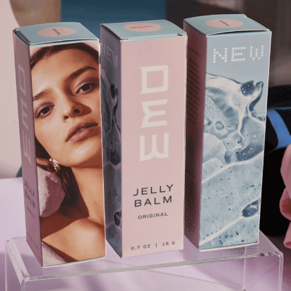 Pastel product packaging on transparent stand showing brand logo, model's face, and abstract design – example of package marketing.