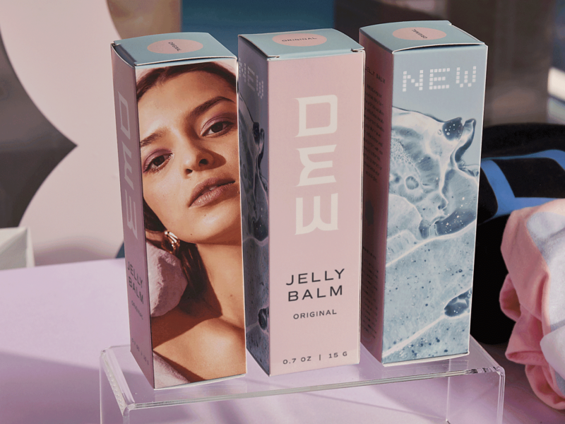 Pastel product packaging on transparent stand showing brand logo, model's face, and abstract design – example of package marketing.